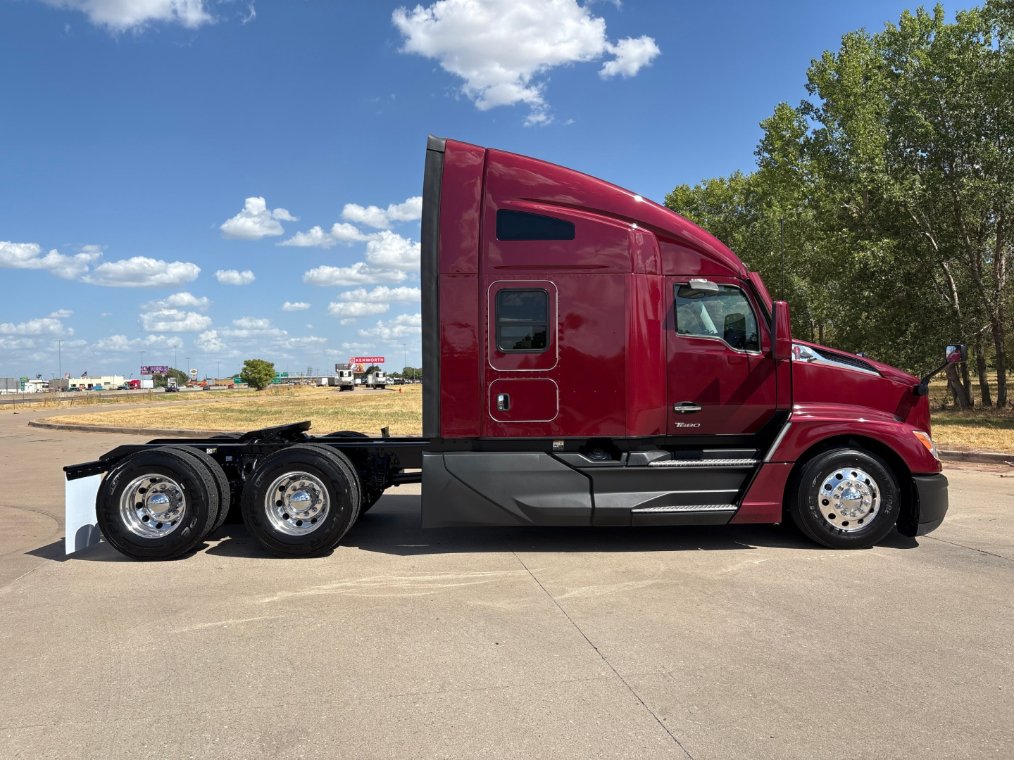 Kenworth T680 tractor unit side view showing red sleeper cab and dual rear axles with chrome wheels.