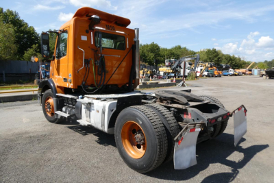 Orange Volvo VNM42T cab and chassis truck with exposed drivetrain and rear fenders in a lot.