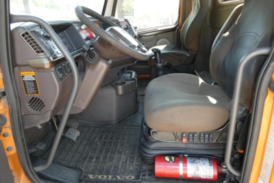 Cab interior of a 2012 Volvo VNM42T truck showing driver seat, steering wheel, dashboard, gear shift, and floor mats.