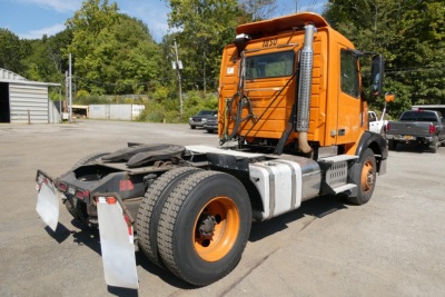 Volvo VNM42T conventional daycab tractor in orange, rear view showing fifth wheel and dual rear tires, VIN and stock notations on cab window.