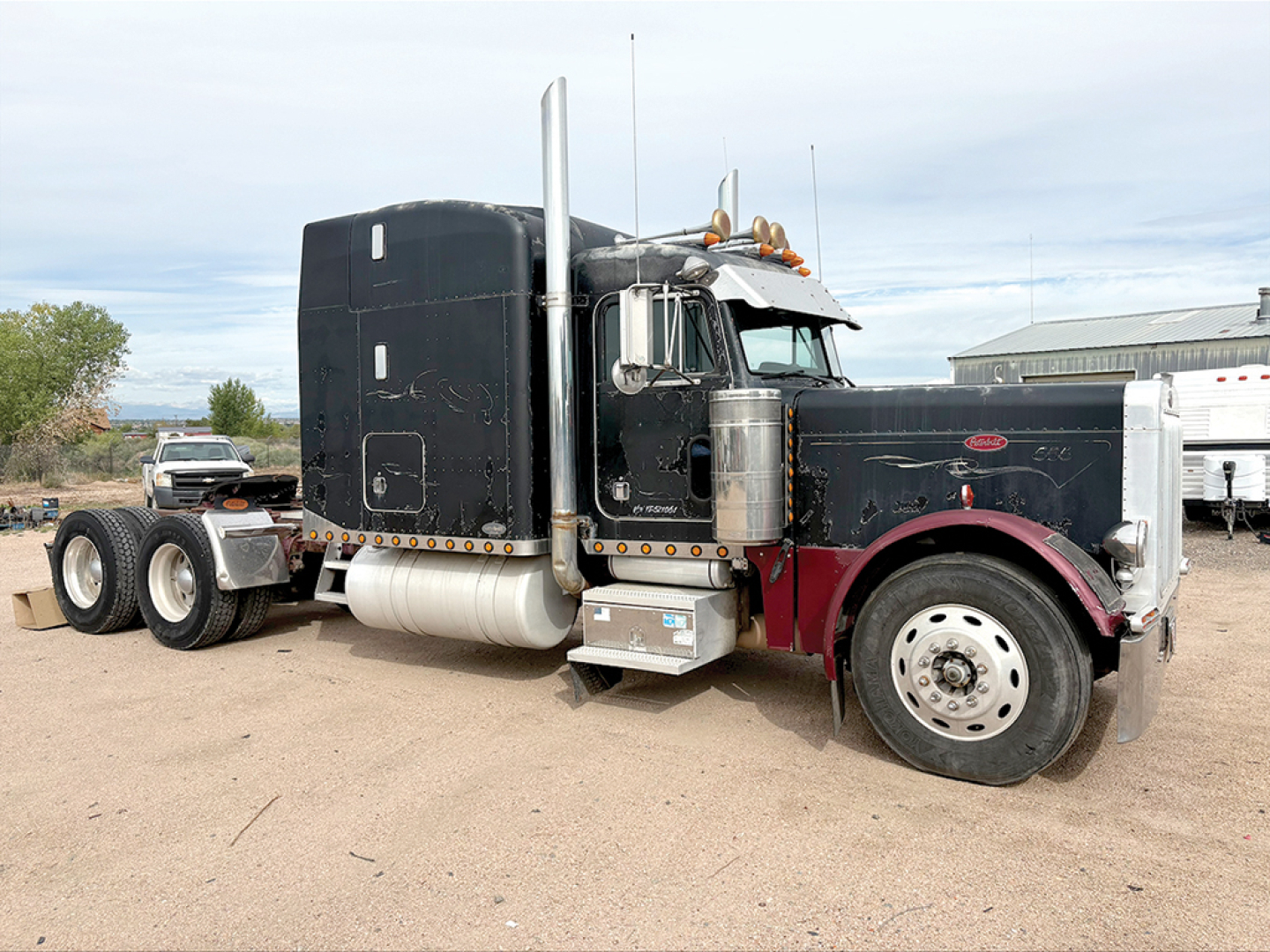Peterbilt 379 UltraCab extended hood tractor in dark color with chrome exhaust stacks, dual rear axles, large front bumper, and sleeper cab.
