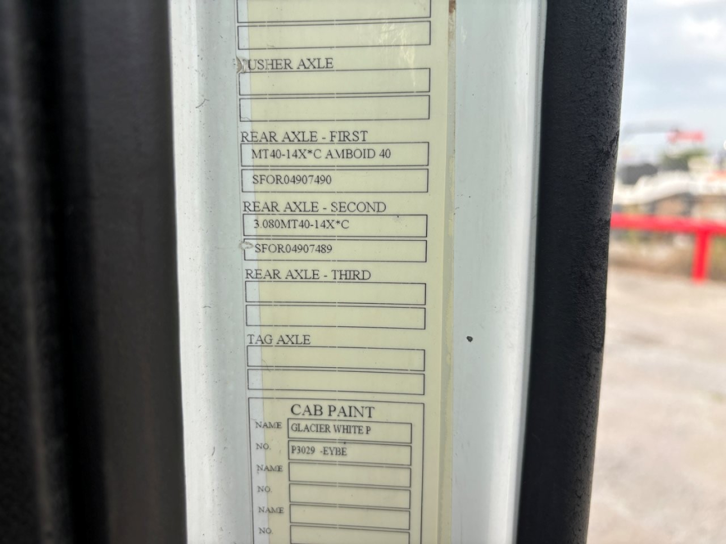 Label with axle specifications and cab paint information on a Volvo VNR truck door jamb; reads MTA 140X-C AMBOID 40, rear axles, tag axle, cab paint GLACIER WHITE P, etc.