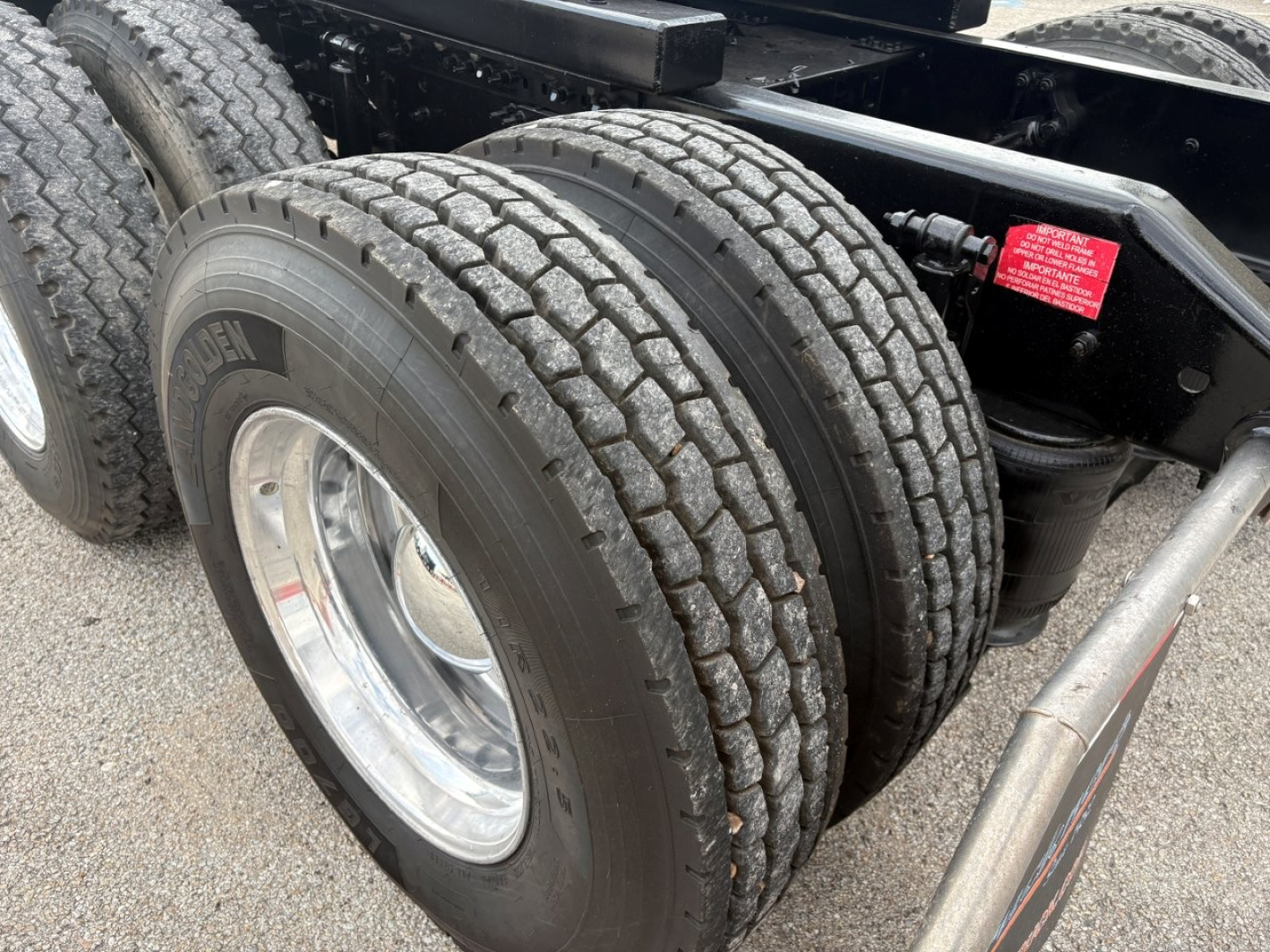 Truck rear dual tires and suspension components of a 2019 Volvo VNR64T640 sleeper cab showing dual tires and chrome wheel, chassis frame, and air suspension with red warning sticker.