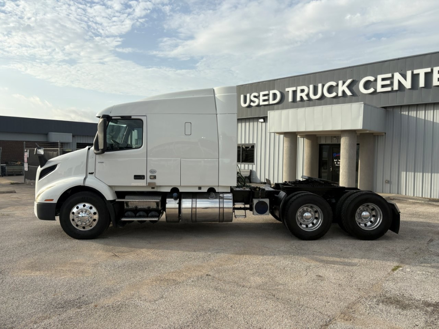Truck chassis and cab of a 2019 Volvo VNR64T640 tractor in front of a Used Truck Center, side view showing semi-truck with sleeper cab.