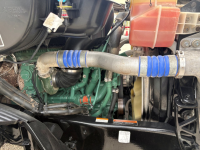 Volvo engine bay showing turbo hoses, green engine block, blue silicone couplers, radiator, and coolant reservoir in cabin area.
