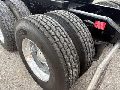 Truck rear dual tires and suspension components of a 2019 Volvo VNR64T640 sleeper cab showing dual tires and chrome wheel, chassis frame, and air suspension with red warning sticker.