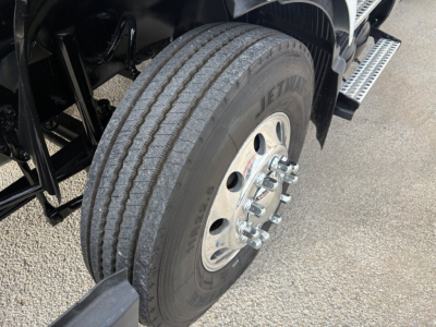 Volvo VNR64T640 truck front wheel area showing dual rear dual tires, polished steel wheel with lug nuts, black frame, step-up side rail.