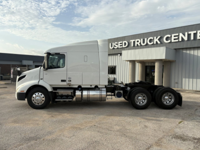 Truck chassis and cab of a 2019 Volvo VNR64T640 tractor in front of a Used Truck Center, side view showing semi-truck with sleeper cab.