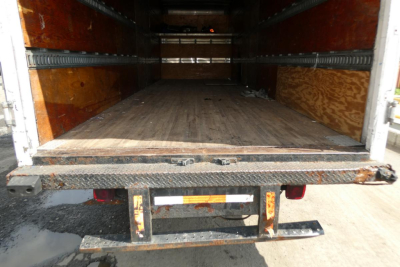 Cargo area of a used 2002 International 4700 box truck showing empty wooden floor, metal side rails, and open rear doors.