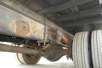 Truck chassis underside showing axle, suspension, and leaf spring with dual rear wheels and rust-free metal frame.