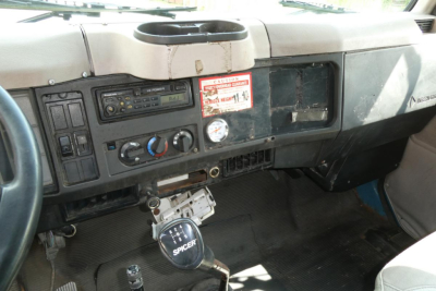 Interior of 2002 International 4700 dashboard with manual transmission shifter and control panel, steering wheel left, stock number sticker, and basic gauges.