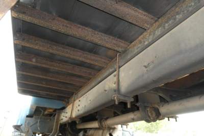Truck undercarriage showing metal frame and suspension components from a 2002 International 4700. Side view focuses on drive axle, leaf spring rails, and underbody structure.