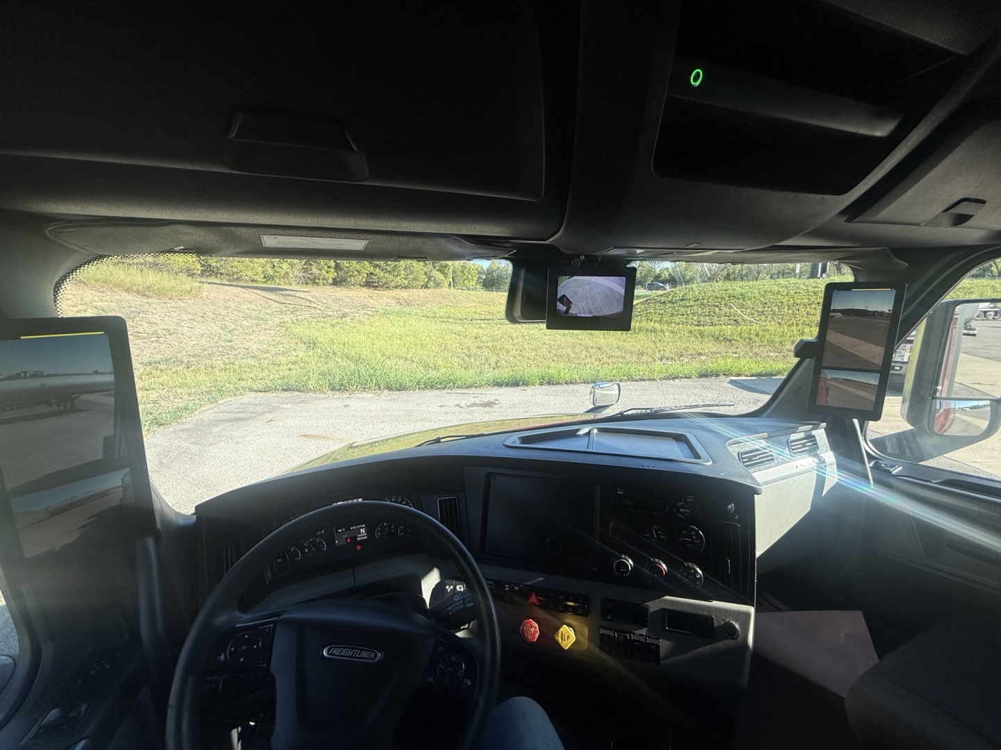 Cab interior of a Freightliner Cascadia 126 truck showing dashboard, steering wheel, side mirrors, and windshield with exterior view