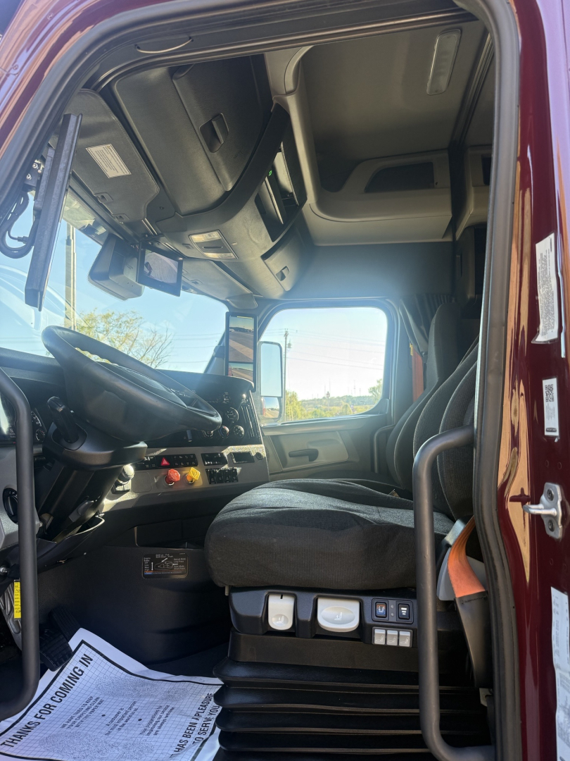 Cab interior of a Freightliner Cascadia 126 truck showing driver seat, dashboard, steering wheel, and door area.