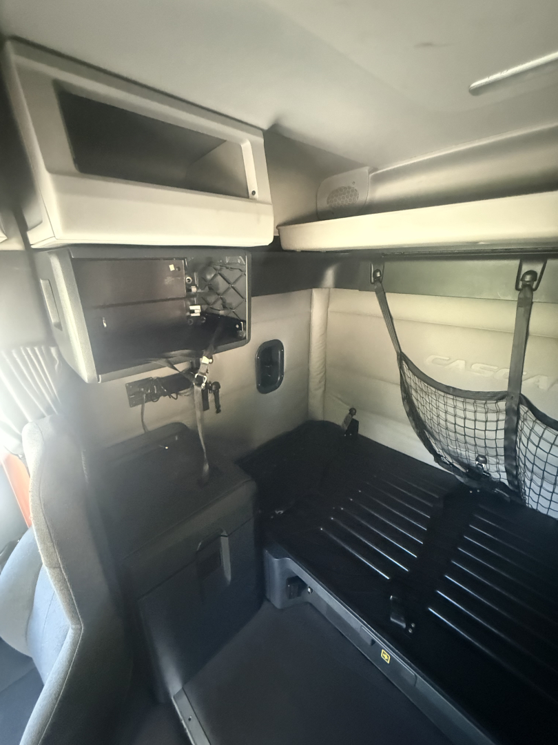 Cab interior of a 2021 Freightliner Cascadia 126 sleeper showing storage cabinets, overhead bunk, and side netting.