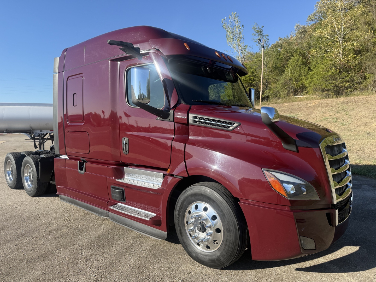 Truck cab: maroon 2021 Freightliner Cascadia 126, side view showing sleeper, chrome steps, dual rear wheels, VIN label not visible, daytime outdoor lot.
