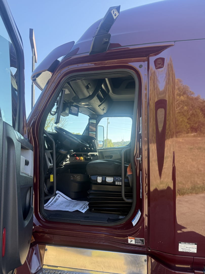 Freightliner Cascadia126 cab interior visible through open door showing steering wheel, dashboard, and driver seat area.