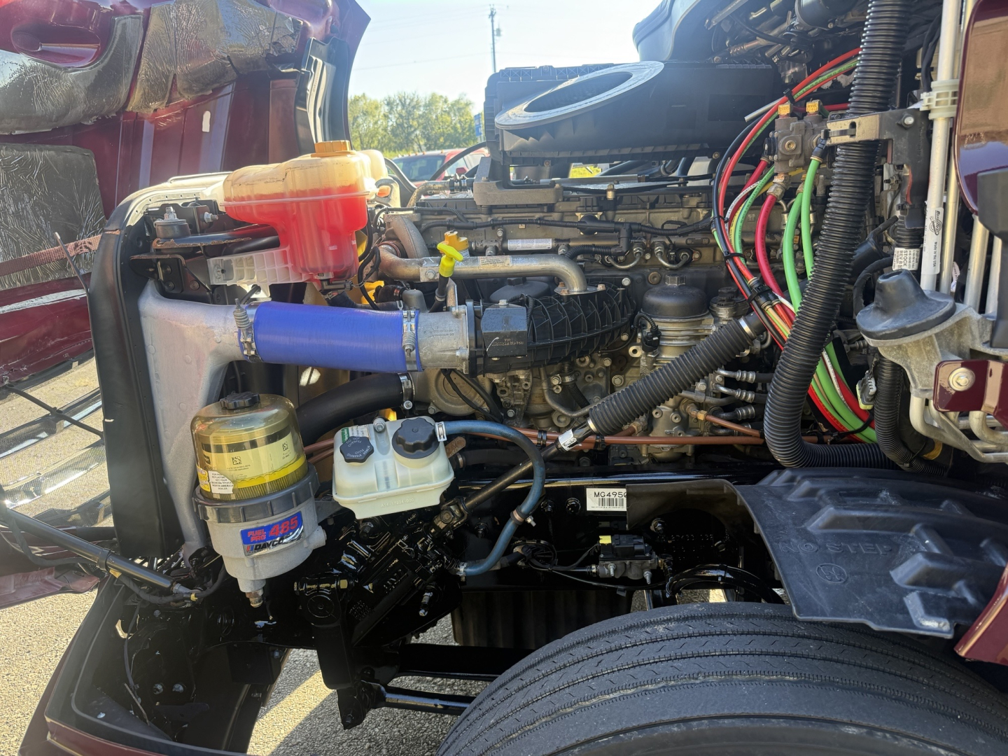 Engine bay of a Freightliner Cascadia126 truck showing coolant reservoir, oil filter, and various colored hoses and wiring harnesses.