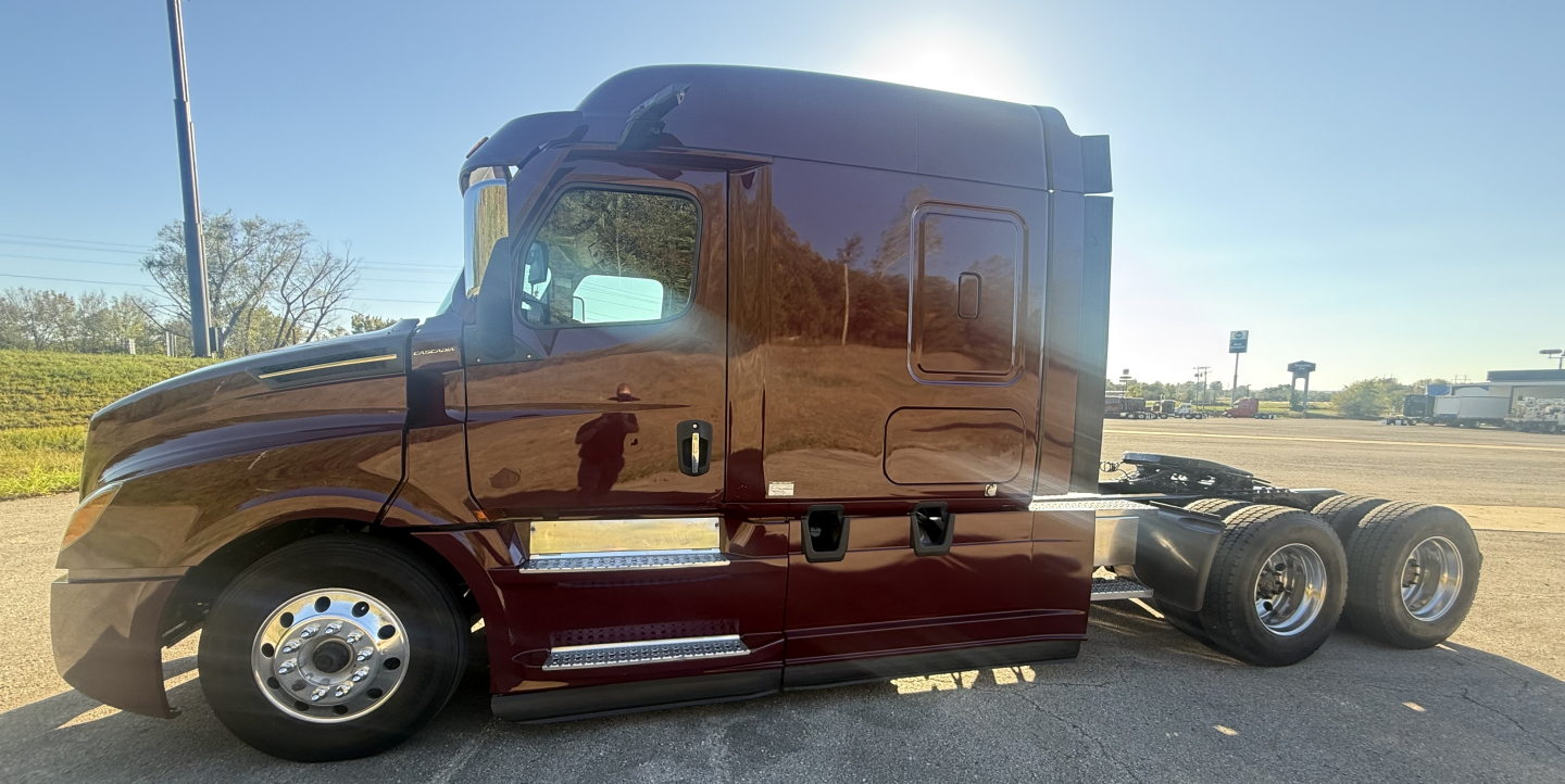 Truck cab side view showing Freightliner Cascadia126 sleeper in brown with chrome steps and dual rear axles.