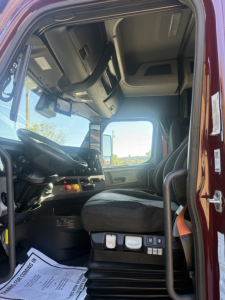 Cab interior of a Freightliner Cascadia 126 truck showing driver seat, dashboard, steering wheel, and door area.