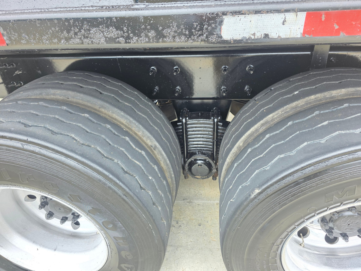 Dump truck rear view showing tandem axle configuration with dual tires and suspension coil springs.