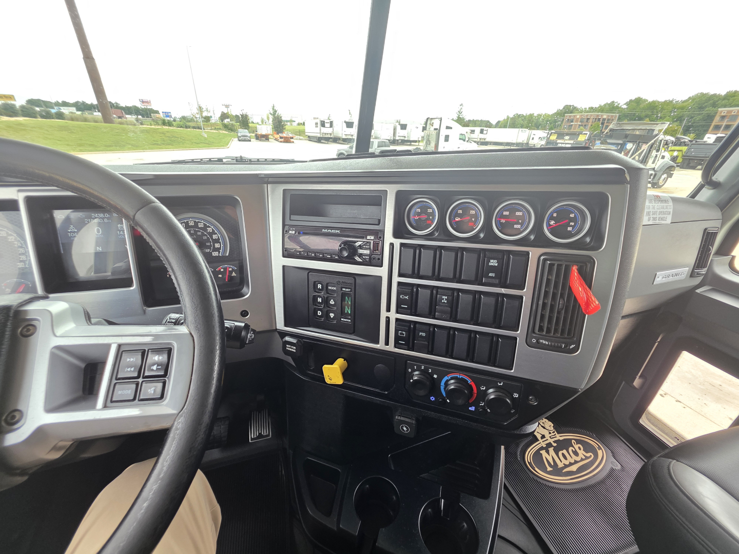 Dashboard view of a Mack Granite truck showing gauge cluster, steering wheel, switches, and center console with yellow tag.