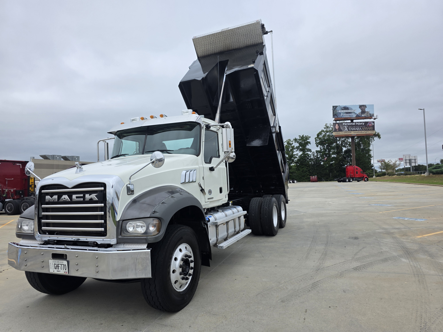 Mack Granite dump truck with raised bed in a parking lot; visible text on the truck includes MACK on the grille and a license plate; no other legible labels.