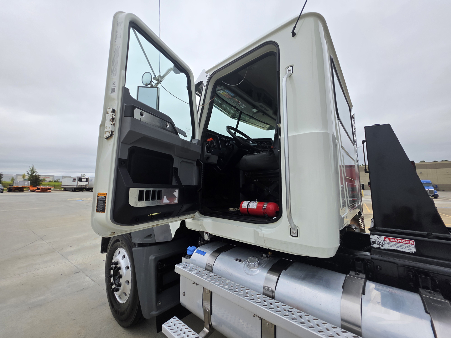 Mack Granite dump truck cab open with driver's door ajar showing interior seating and steering wheel, large undecorated metal fuel tank beneath, and dumping body partially visible