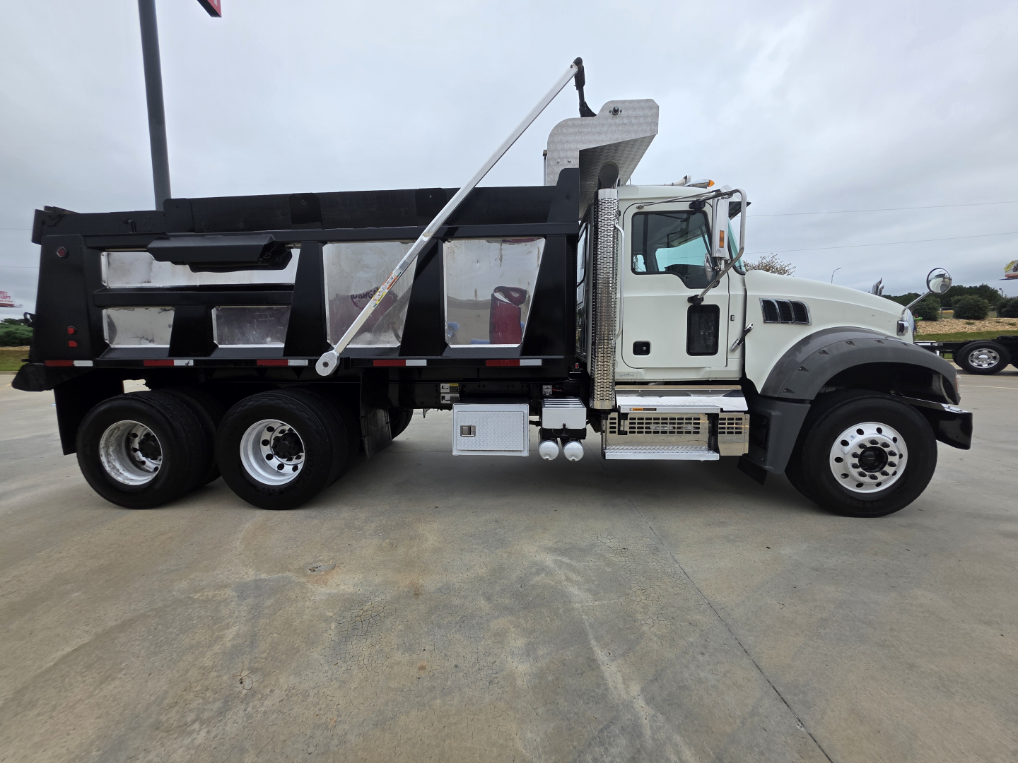 Truck side view showing a Mack GRANITE dump truck with a black dump body and white cab, VIN plate area not legible.
