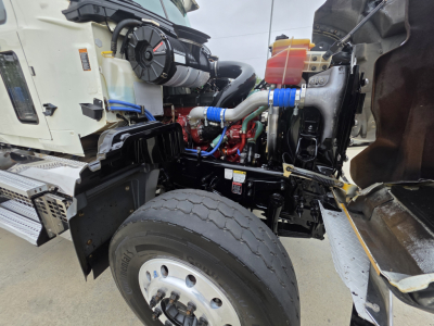 Mack Granite truck engine bay view showing coolant reservoir, blue silicone hoses, red engine components, black frame, aluminum steps, and front wheel in foreground.