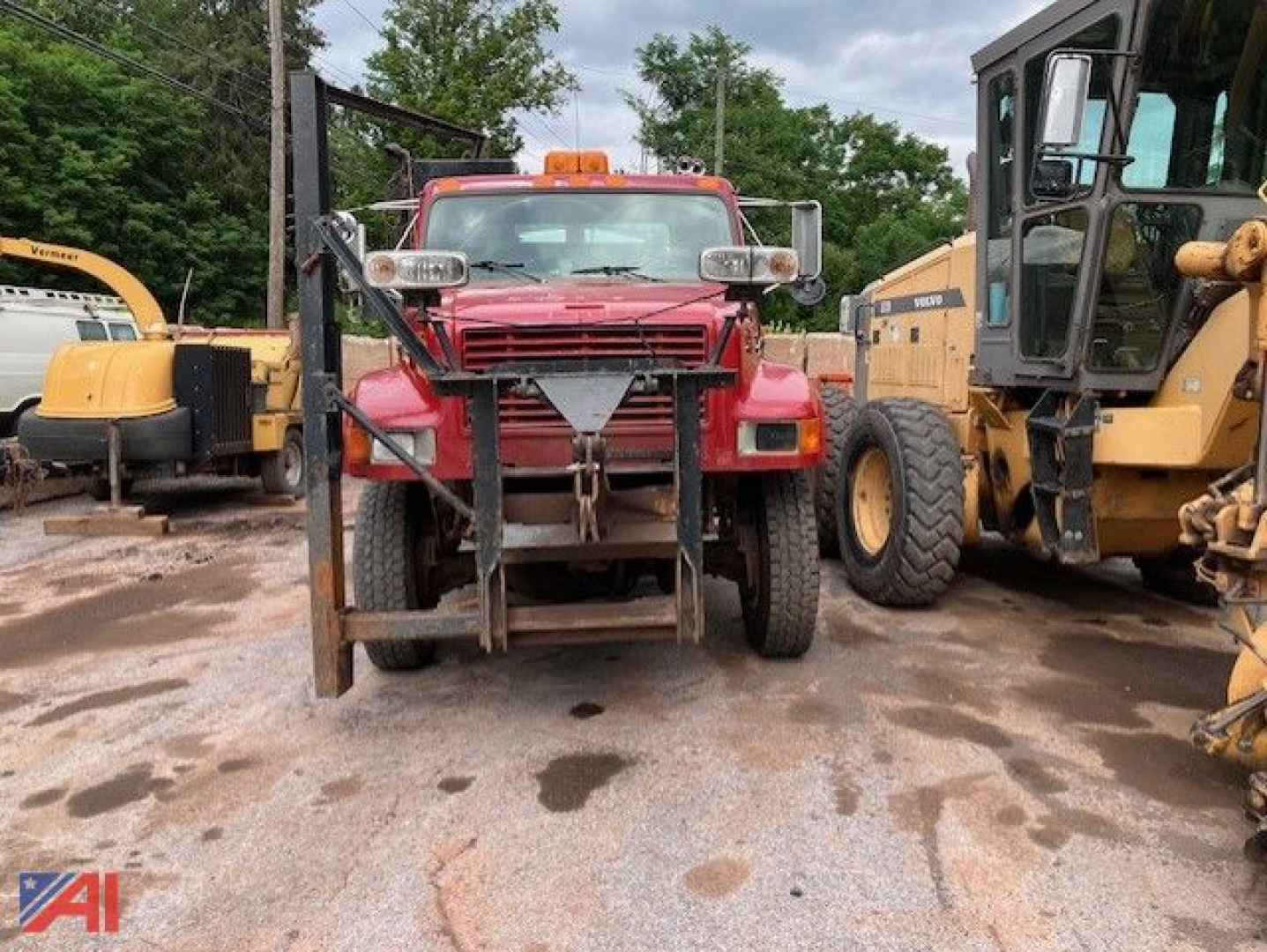 Front view of a red 1995 International 4800 stake dump truck with utility lights on cab, other heavy equipment flanking on both sides