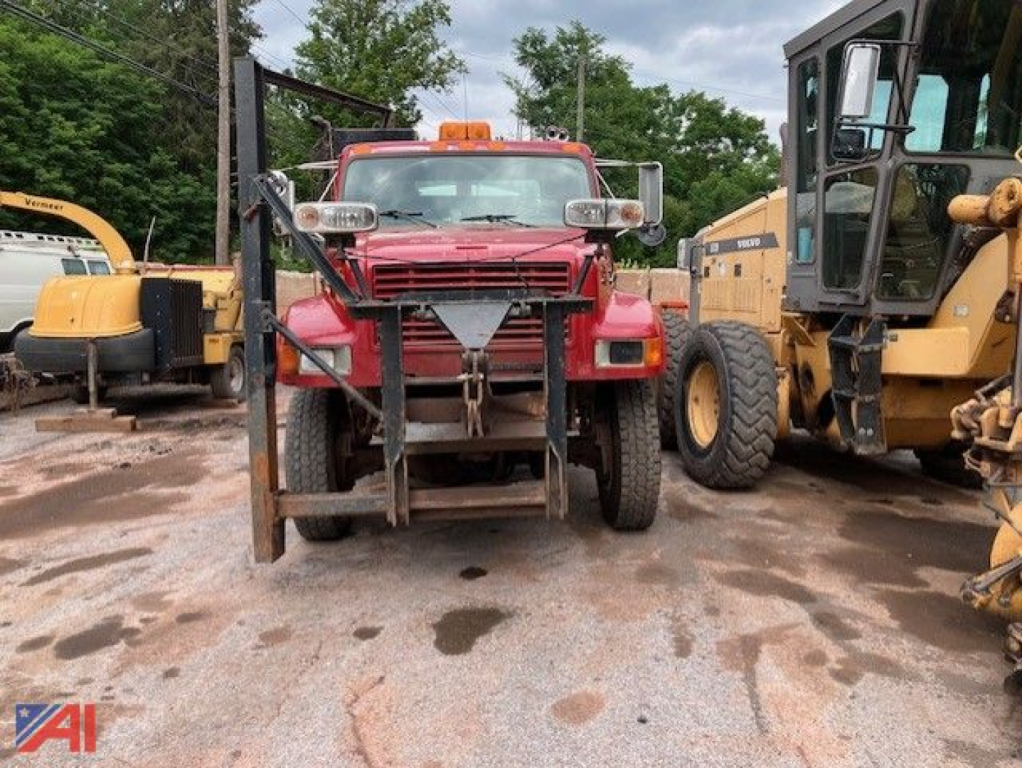 Front view of a red 1995 International 4800 stake dump truck with utility lights on cab, other heavy equipment flanking on both sides