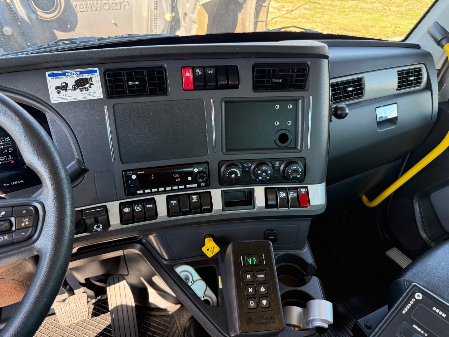 Kenworth T880 truck cabin interior showing dashboard with switches, center console, HVAC dials, and steering wheel; visible gear selector and cup holders.