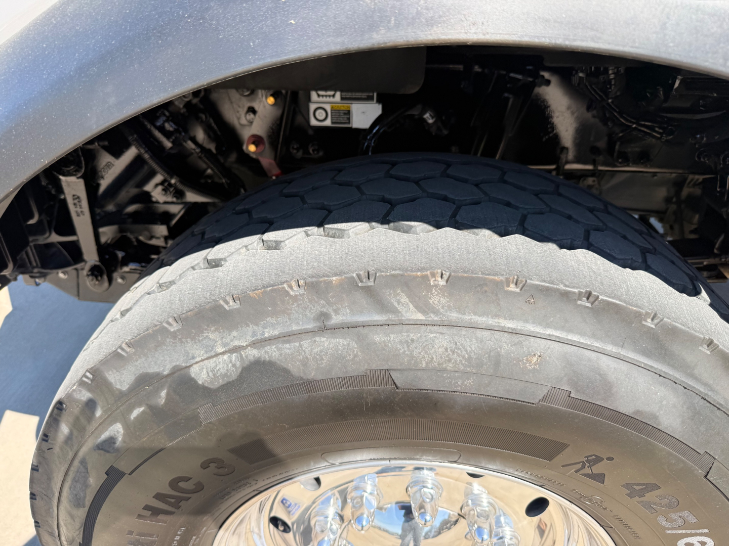 Kenworth T880 truck front wheel area showing large tire with visible tread and wheel, undercarriage components and fender in view.