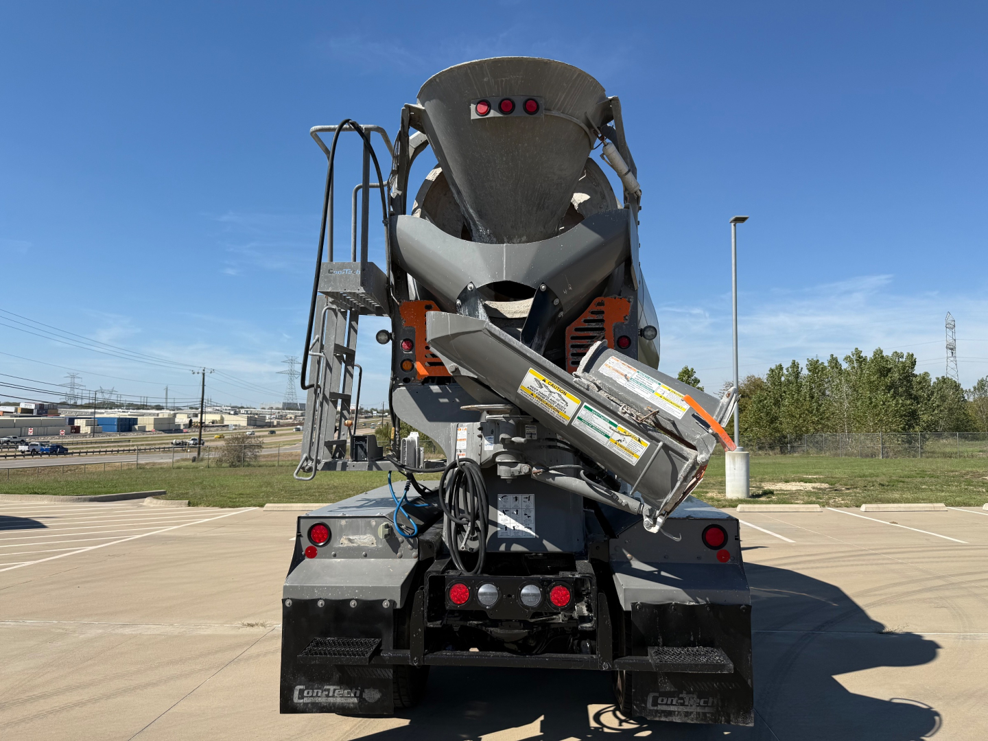 Kenworth T880 mixer truck rear view showing concrete chute and hydraulic system with warning decals.