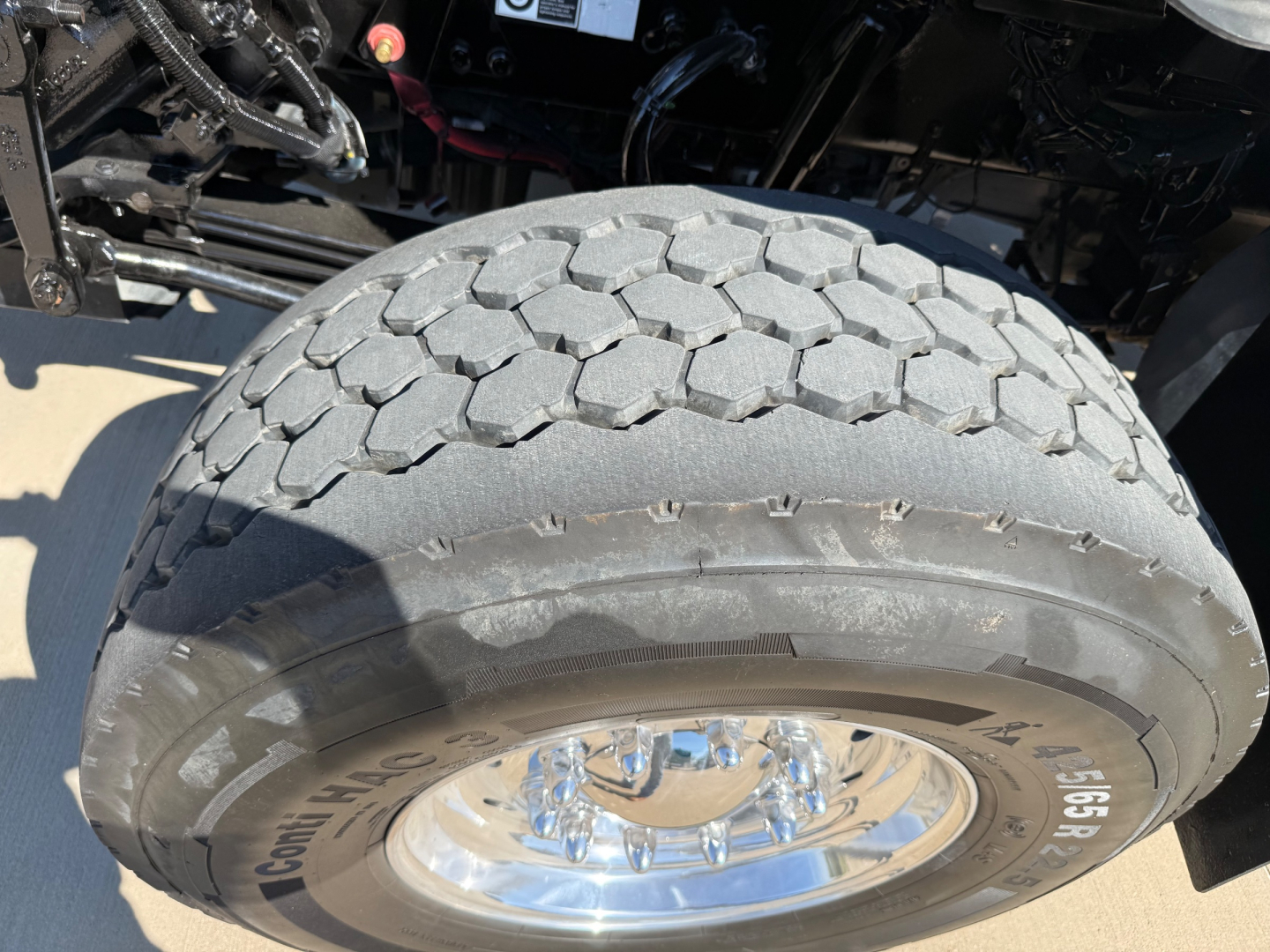 Kenworth T880 wheel and tire close-up showing large tread with hexagonal pattern. Visible are spare components and chrome wheel with lug nuts.