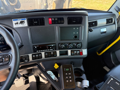 Kenworth T880 truck cabin interior showing dashboard with switches, center console, HVAC dials, and steering wheel; visible gear selector and cup holders.