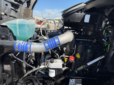 Kenworth T880 engine bay with coolant reservoir, hoses, and various hydraulic lines visible; intake tubing and battery area partially seen.