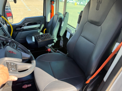 Kenworth T880 mixer truck interior showing black fabric seats, yellow steering wheel accent, dashboard with control panel, and orange seat belt. Driver seat and passenger area visible.