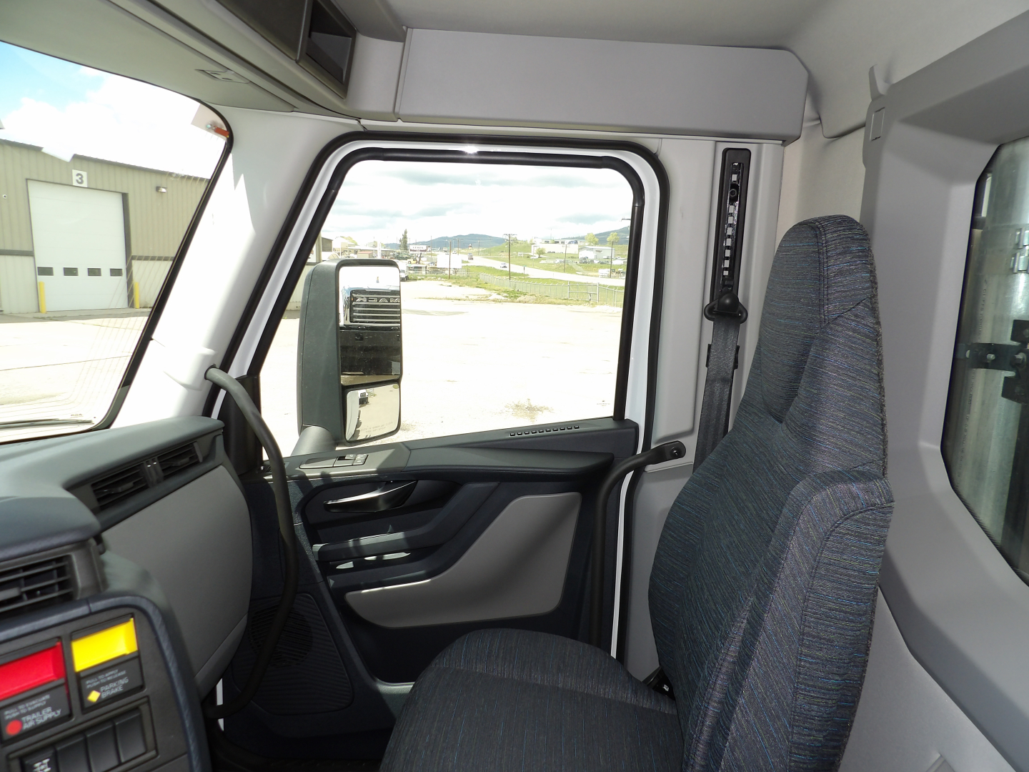 Truck cab interior showing steering wheel, door panel, and side mirror; visible window and seat.