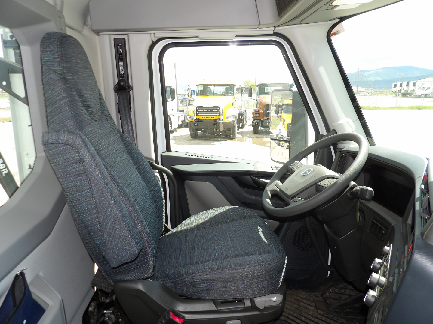 Driver cabin of a new Volvo VNL64T300 cab showing steering wheel and seat with view through the windshield to other trucks.