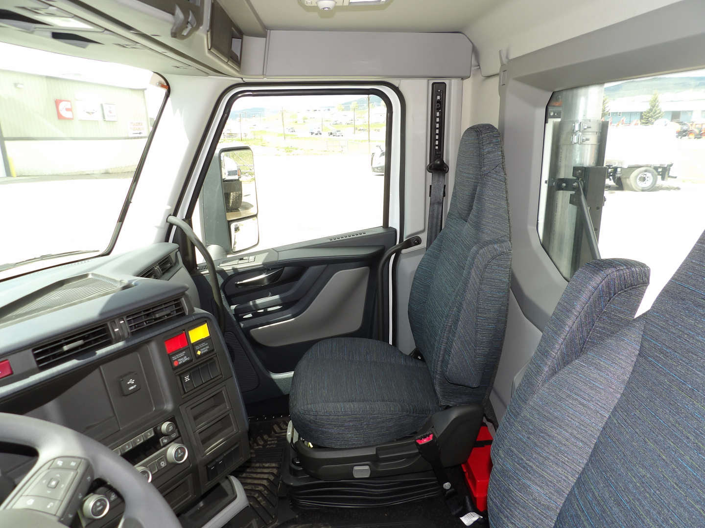  Volvo VNL64T300 cab interior showing steering wheel, driver seat, dashboard, and door with controls; view through windshield to exterior.