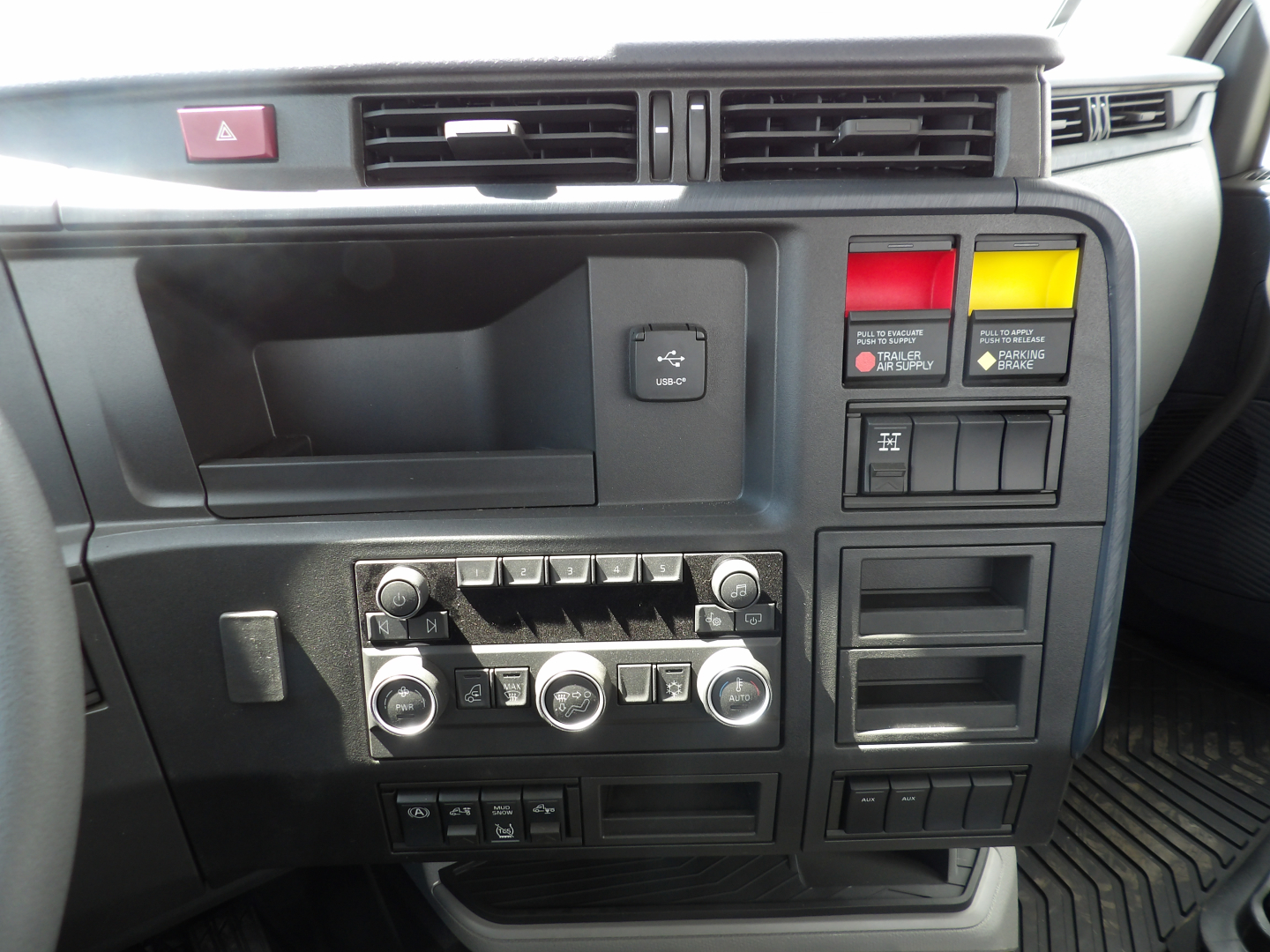 Volvo VNL64T300 interior dash showing climate controls, hazard switch, two colored warning buttons, and multiple control panels; visible text includes various unlabeled buttons and knobs.