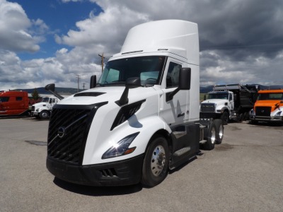 Volvo VNL64T300 conventional daycab truck in white, front three-quarter view with high sleeper, other trucks in background.