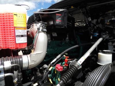 Volvo truck engine bay showing coolant reservoir with yellow warning label and surrounding hoses and components.