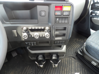Interior cab area of a Volvo VNL64T300 showing dashboard controls, climate dials, switches, pedals, and center console.