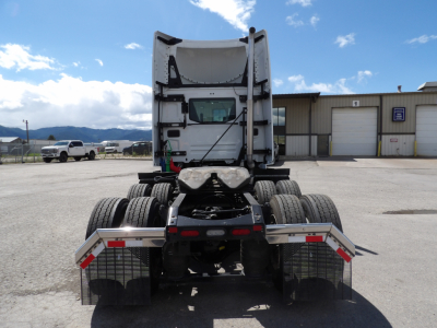 Truck tractor rear view showing fifth wheel, dual rear axles, and side guards with reflective tape in a dealership lot.
