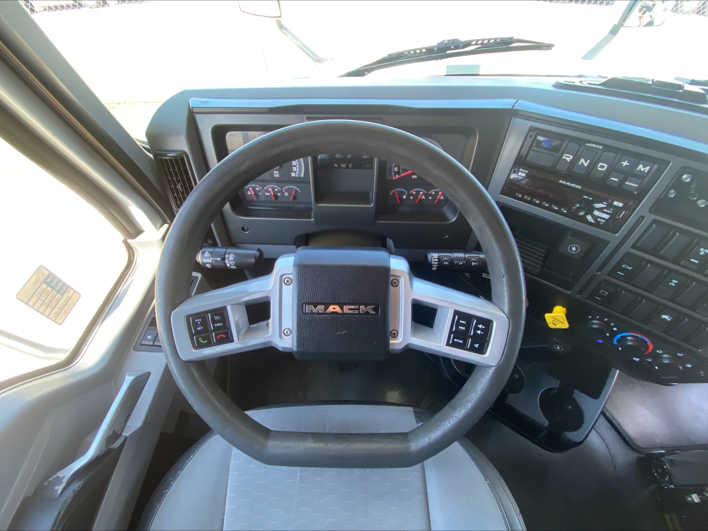 Dashboard and steering wheel of a 2019 Mack AN64T70 truck cab interior with Mack logo on center of steering wheel.