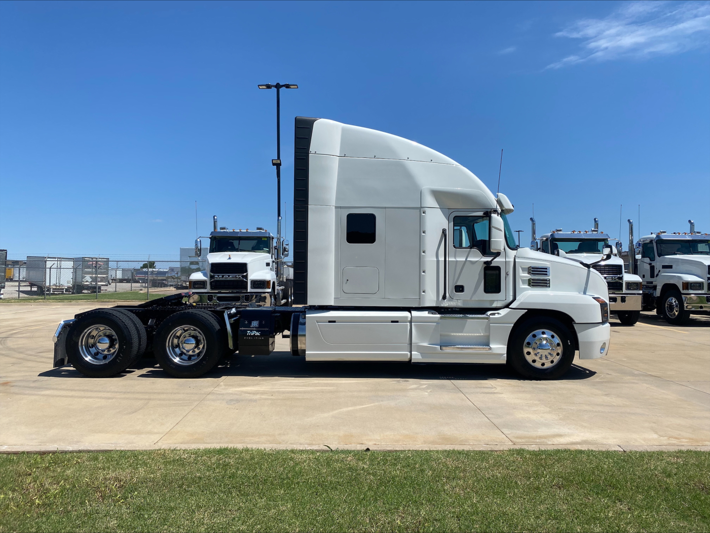 Truck side view of a 2019 Mack AN64T70 conventional sleeper, showing a long hood, sleeper cab, and dual rear axles on a concrete lot.