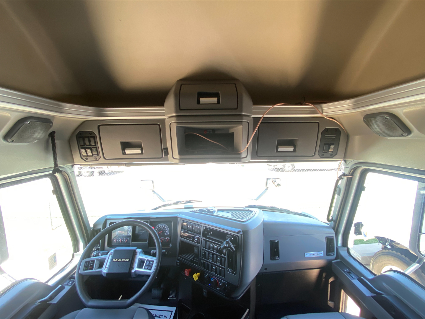 Truck cab interior showing Mack AN64T70 dashboard and steering wheel with overhead storage compartments.